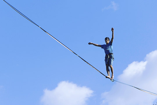 looking up at a tight rope walker against a blue sky